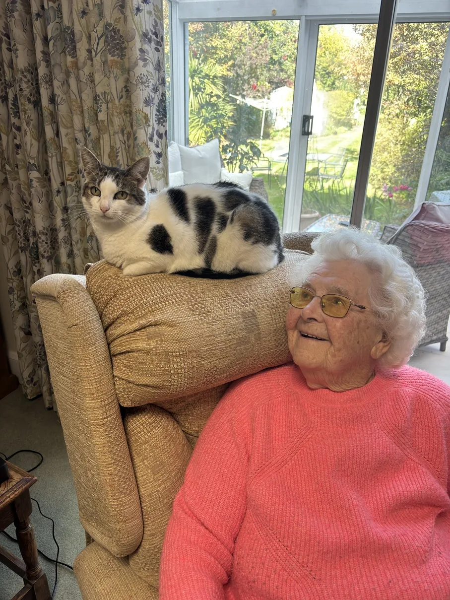Olga Hopkins at home with a cat resting on the back of her chair.