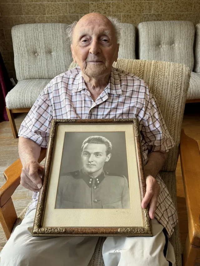 Andor Mohos holding a framed portrait of himself in military uniform.