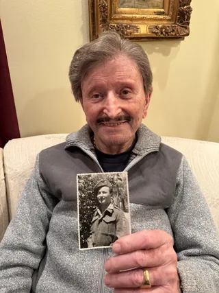 David Karmi holding a photograph of himself in military uniform.