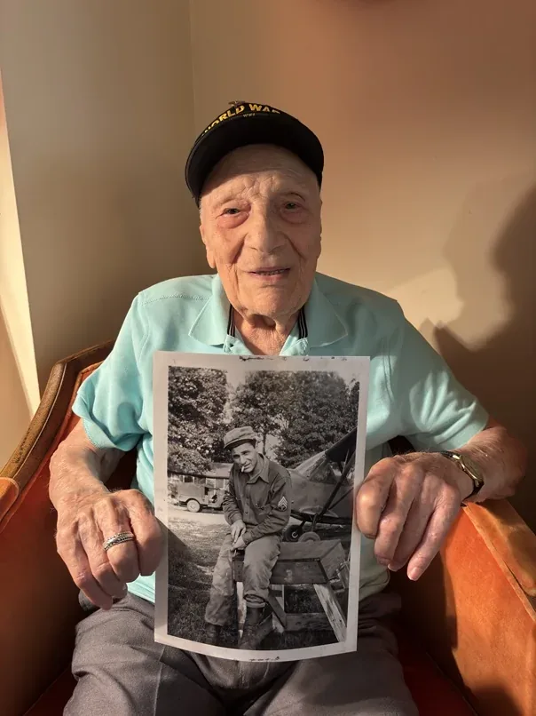 Dominick Critelli holding a historical photograph of himself during his military service.