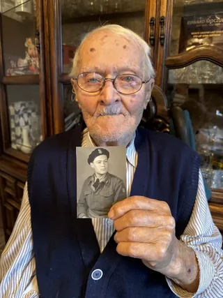 Edward Moczulski holding a photograph of himself in Polish military uniform.