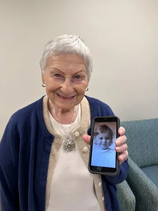 Eva Perlman holding a phone displaying a photograph of herself as a child.