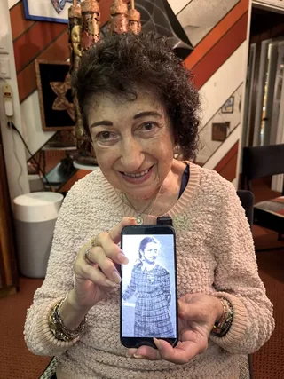 Gabriella Karin holding a phone displaying a photograph of herself as a child.