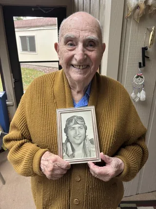 George Rubin holding a framed portrait of himself as a young airman.