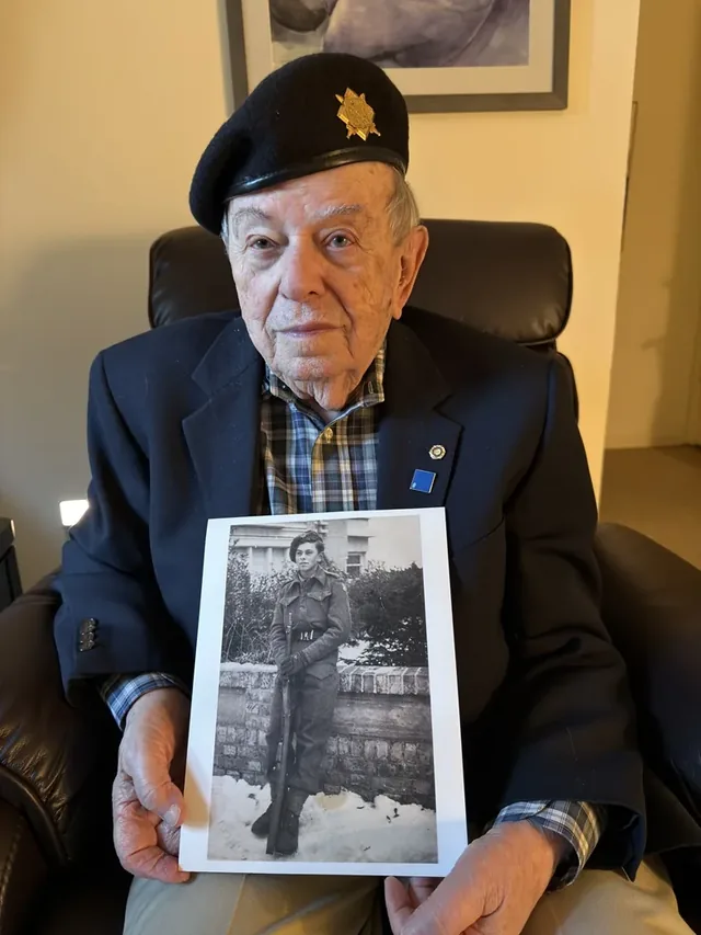 Harry Arnstein holding a photograph of himself during his military service.