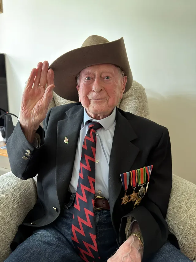 James Fenton saluting while wearing his slouch hat and military medals.