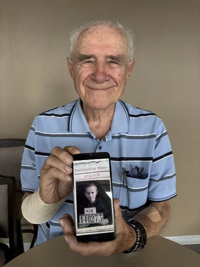 Lech Gade holding a phone displaying his prisoner-of-war photograph.