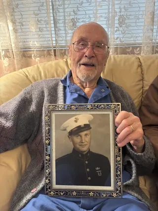 Lee Robinson holding a framed photograph of himself in United States Marine Corps uniform.