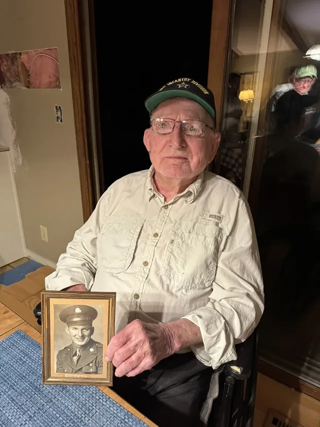 Melvin Voltz holding a framed photograph of himself in United States Army uniform.