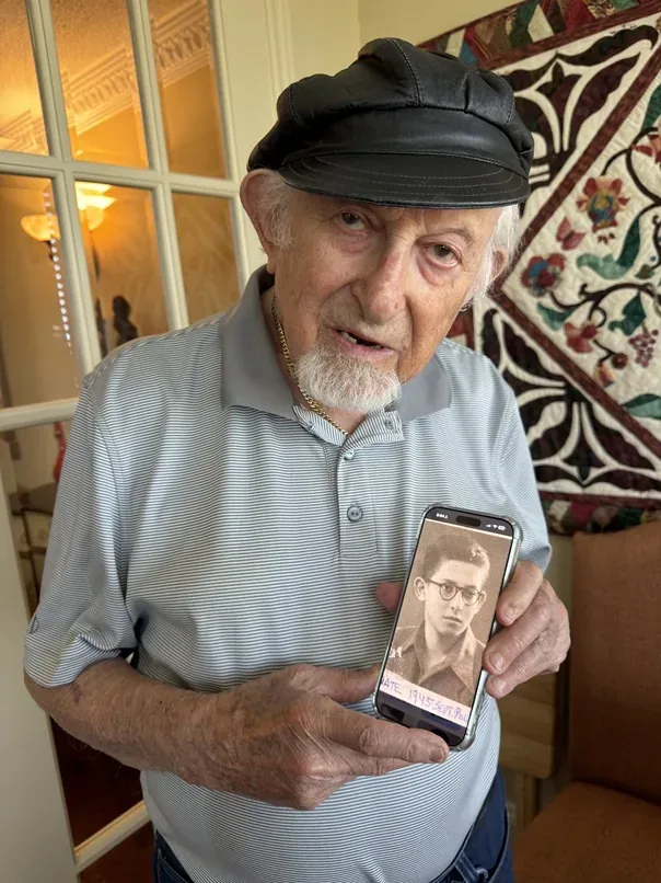 Nate Leipciger holding a phone displaying a photograph of himself as a young man.