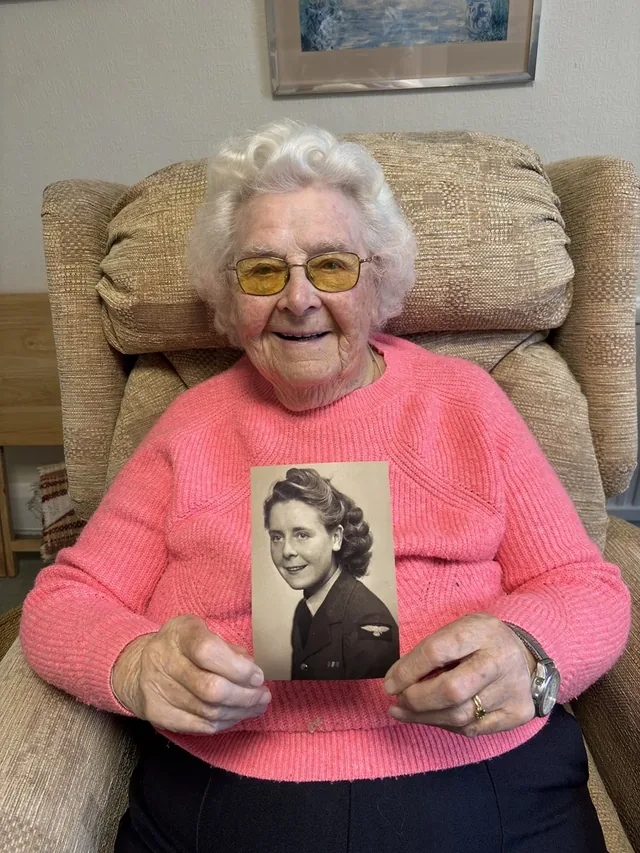 Olga Hopkins holding a photograph of herself in WAAF uniform.