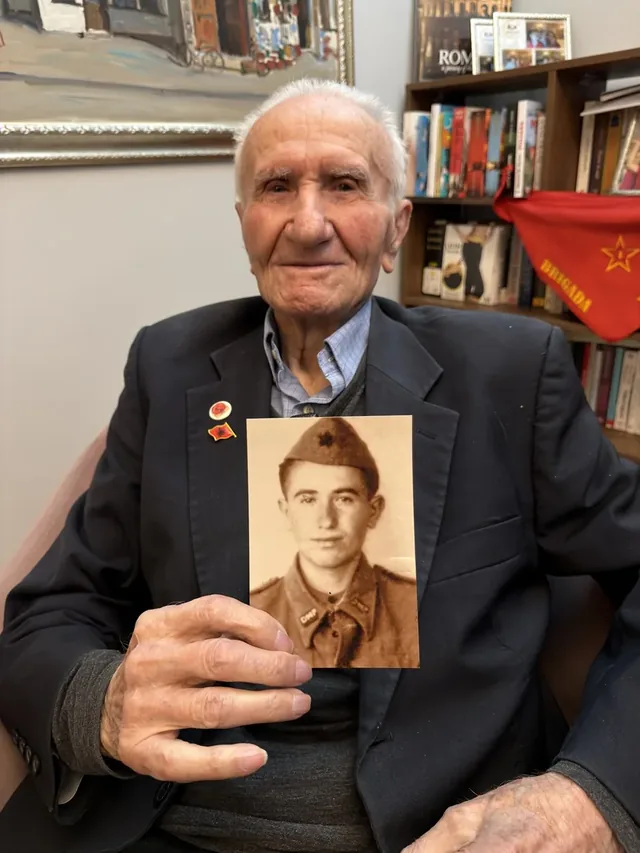 Qemal Bego holding a photograph of himself in military uniform.