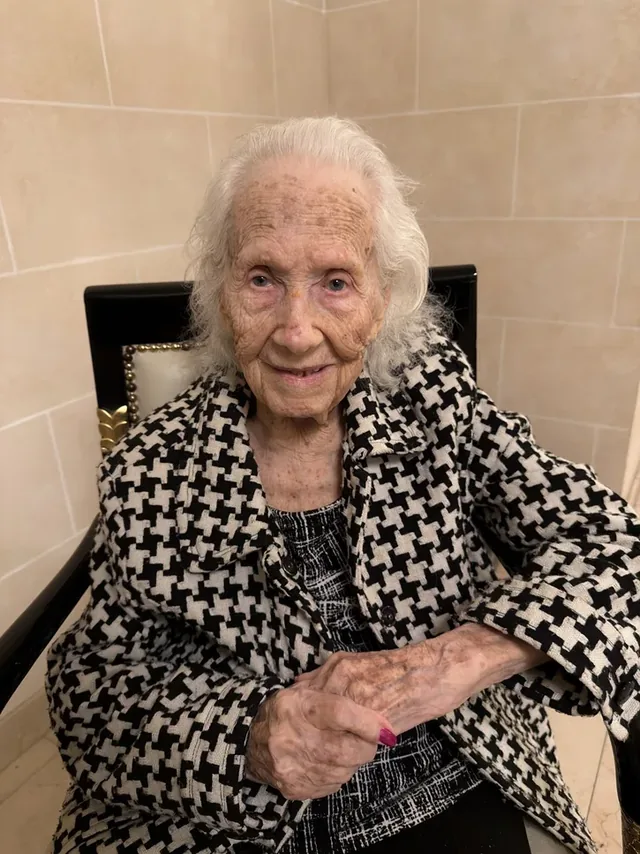 Renée Firestone seated in a patterned coat.