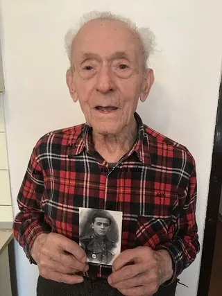 Štefan Šteflovič holding a photograph of himself in military uniform.