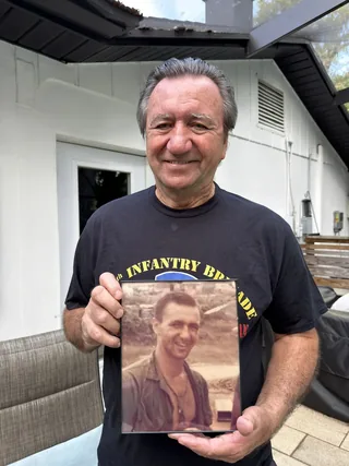 Stephen Kochick holding a photograph of himself during his military service.