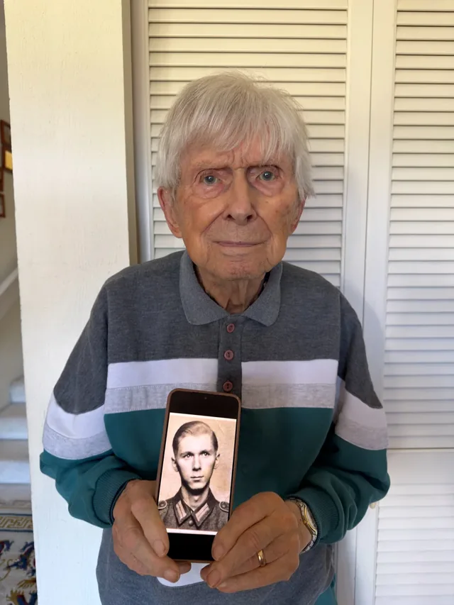 Wolfram Forster holding a phone displaying a photograph of himself in military uniform.